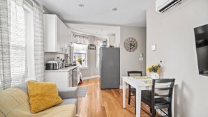 A modern kitchen with white cabinets, a grey refrigerator, and a dining area with a white table and chairs.
