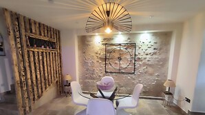 A dining area with a round table and four white chairs, a wooden wall with a rustic design, a modern light fixture, and a textured wall with a circular design.