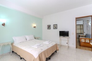 A bedroom with a bed, a television on a stand, a small table, and a door leading to another room.