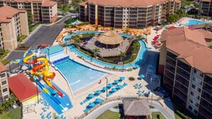 Un complexe hôtelier doté d’une piscine centrale, d’un toboggan aquatique et de plusieurs bâtiments avec balcons.