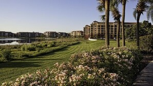 Un hôtel doté d’une pelouse bien entretenue, de palmiers et d’une étendue d’eau en arrière-plan.