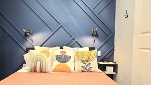 A bedroom with a bed, pillows, a nightstand, and a wall with a geometric pattern.