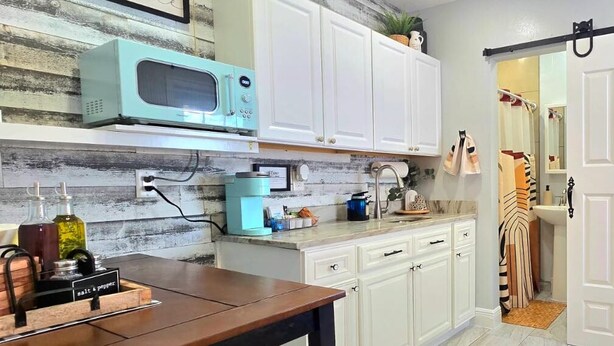A kitchen with white cabinets, a teal microwave, a coffee machine, and a refrigerator.