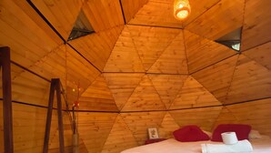 Una habitación acogedora de madera con forma triangular, con una cama, una mesita y una lámpara colgante.