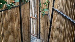 Un estrecho pasillo delimitado por una valla de bambú, con suelo de piedra, que conduce a una zona central.