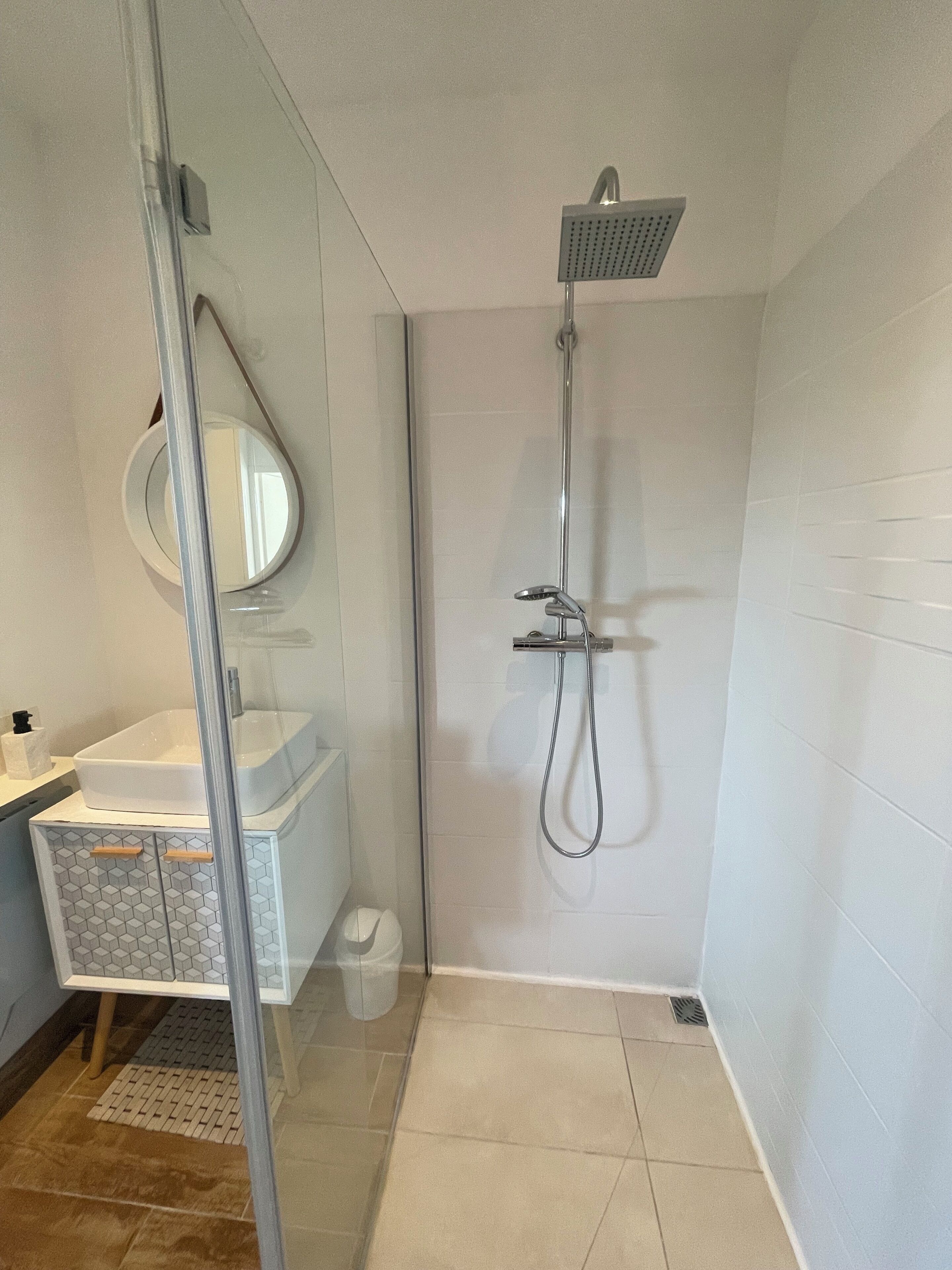 Een moderne badkamer met een douchecabine van glas, een witte wastafel en een spiegel.