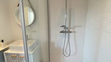 Een moderne badkamer met een douchecabine van glas, een witte wastafel en een spiegel.