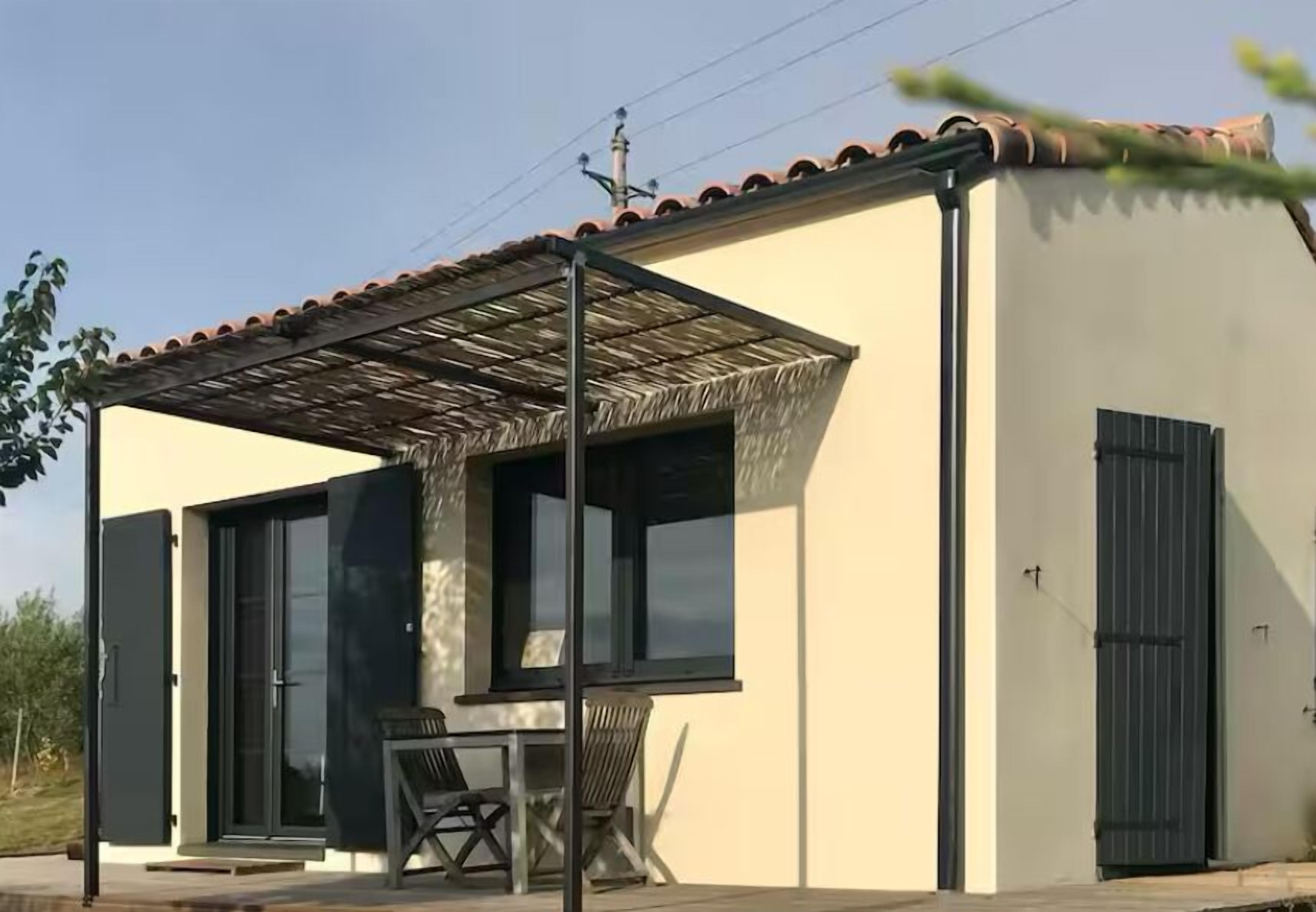 Ein modernes Gebäude mit überdachter Terrasse, großen Fenstern und einer Tür.