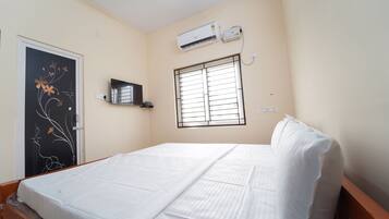 Una cama bien hecha en una habitación con ventana, un equipo de aire acondicionado y un estante en la pared.