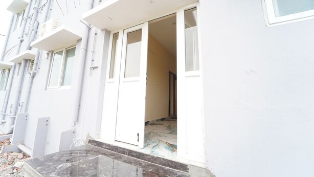 A building with multiple windows and a door, some of which are open. There are visible pipes and a tiled floor.