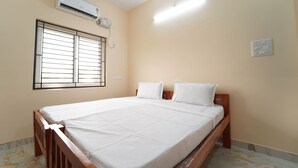 A bedroom with a bed, air conditioning unit, window, and wall socket.