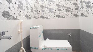 A small bathroom with a toilet, a shower, and a toilet paper holder. - Medhaa Homes Madurai (Madurai)