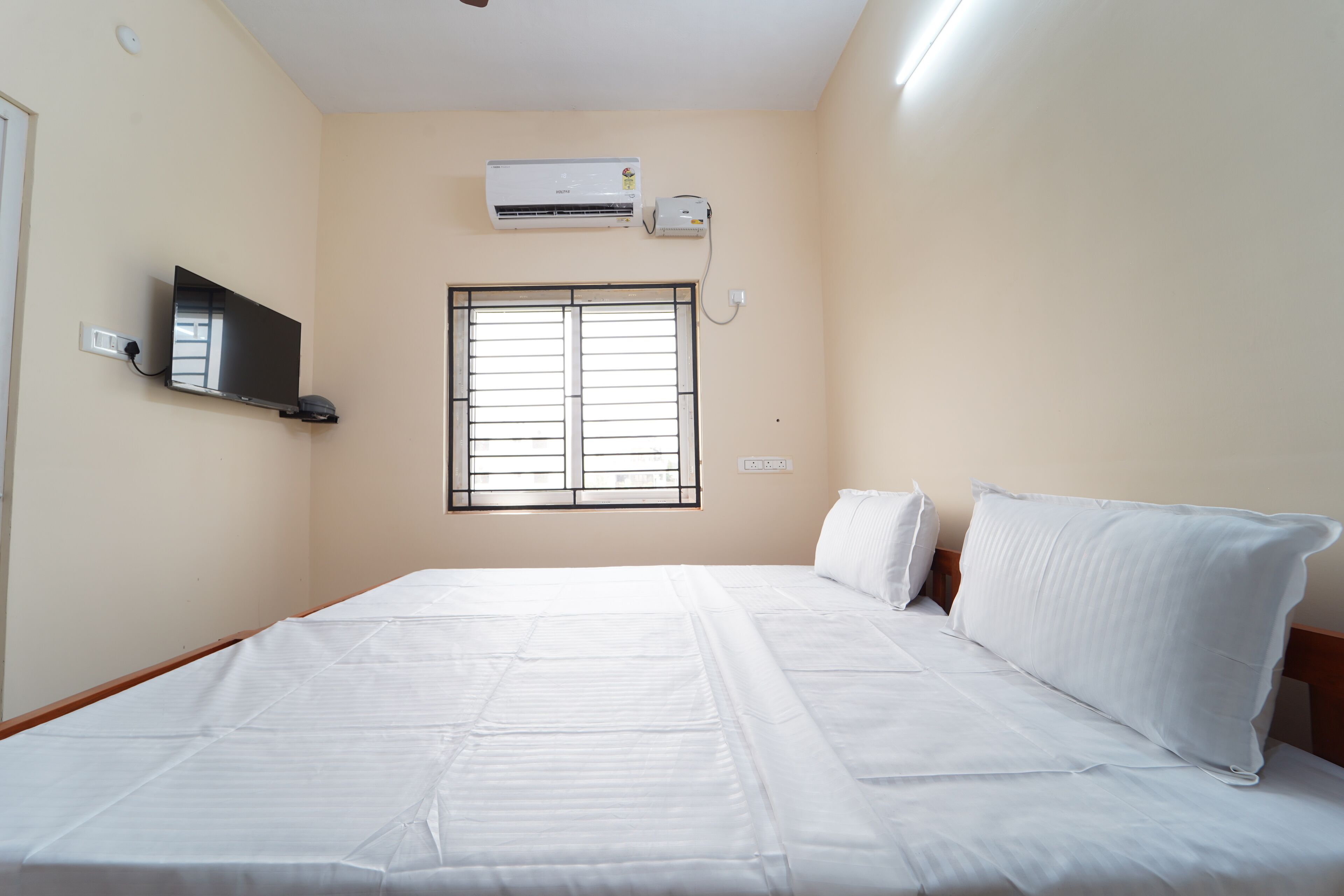 A bedroom with a bed, a TV, an air conditioner, and a window.