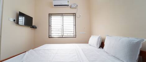 A bedroom with a bed, a TV, an air conditioner, and a window.