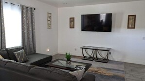 A modern living room with a sofa, a glass coffee table, and a flat-screen TV mounted on the wall.