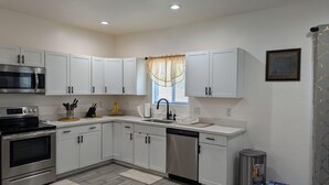 A modern kitchen with white cabinetry, stainless steel appliances, and a window with a sheer curtain.