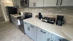 A modern kitchen with grey cabinets, a stainless steel refrigerator, a microwave, a kettle, and a coffee maker.