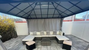 An outdoor seating area with a covered section, cushioned benches, and a central table.