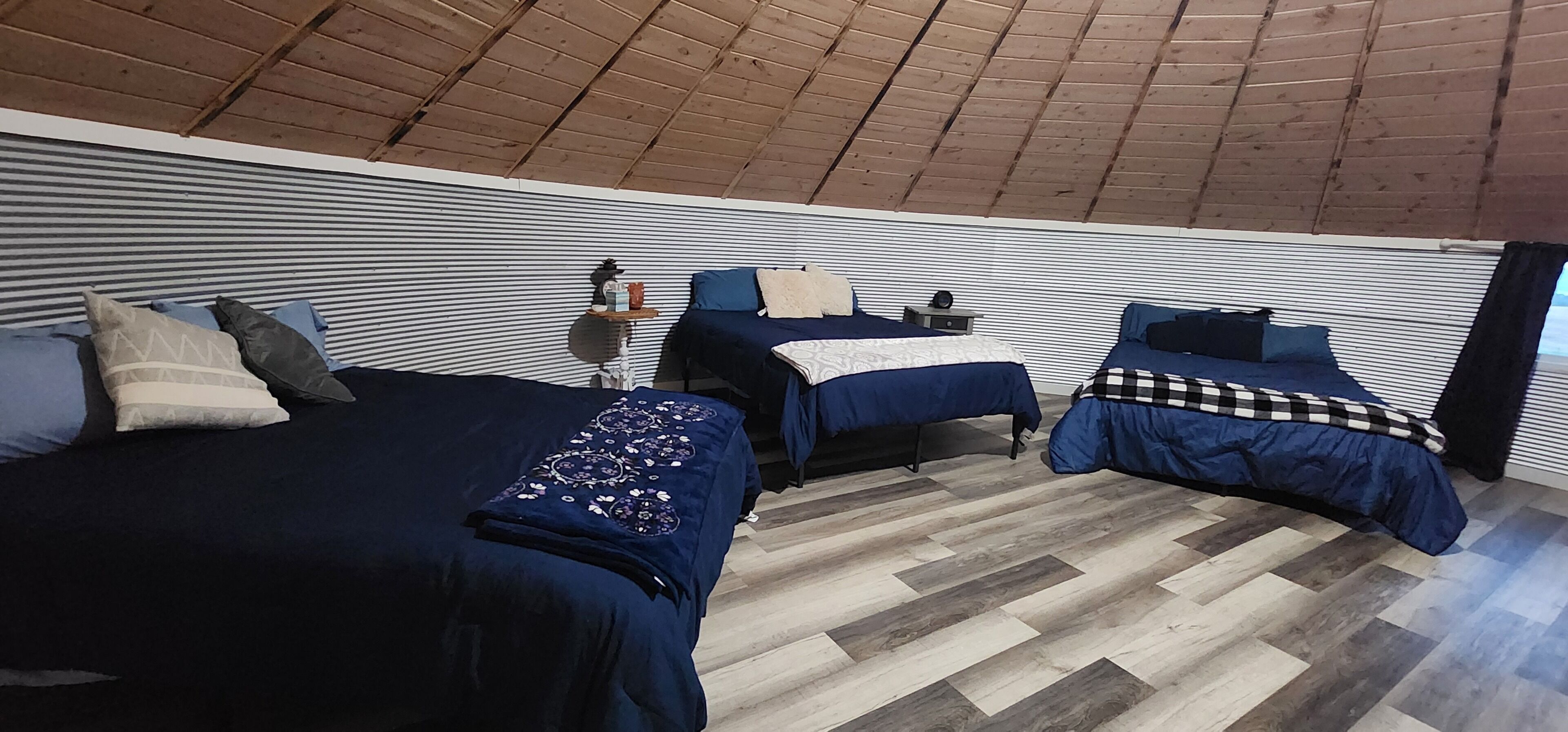 Una habitación acogedora con tres camas, techo de madera y pared a rayas.