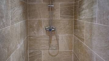 Ducha con cabezal de lluvia y ducha de mano, paredes con azulejos y suelo de mosaico.