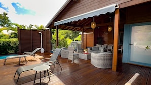 Une terrasse extérieure avec un plancher en bois, des meubles en osier et une porte vitrée donnant accès à une zone piscine.