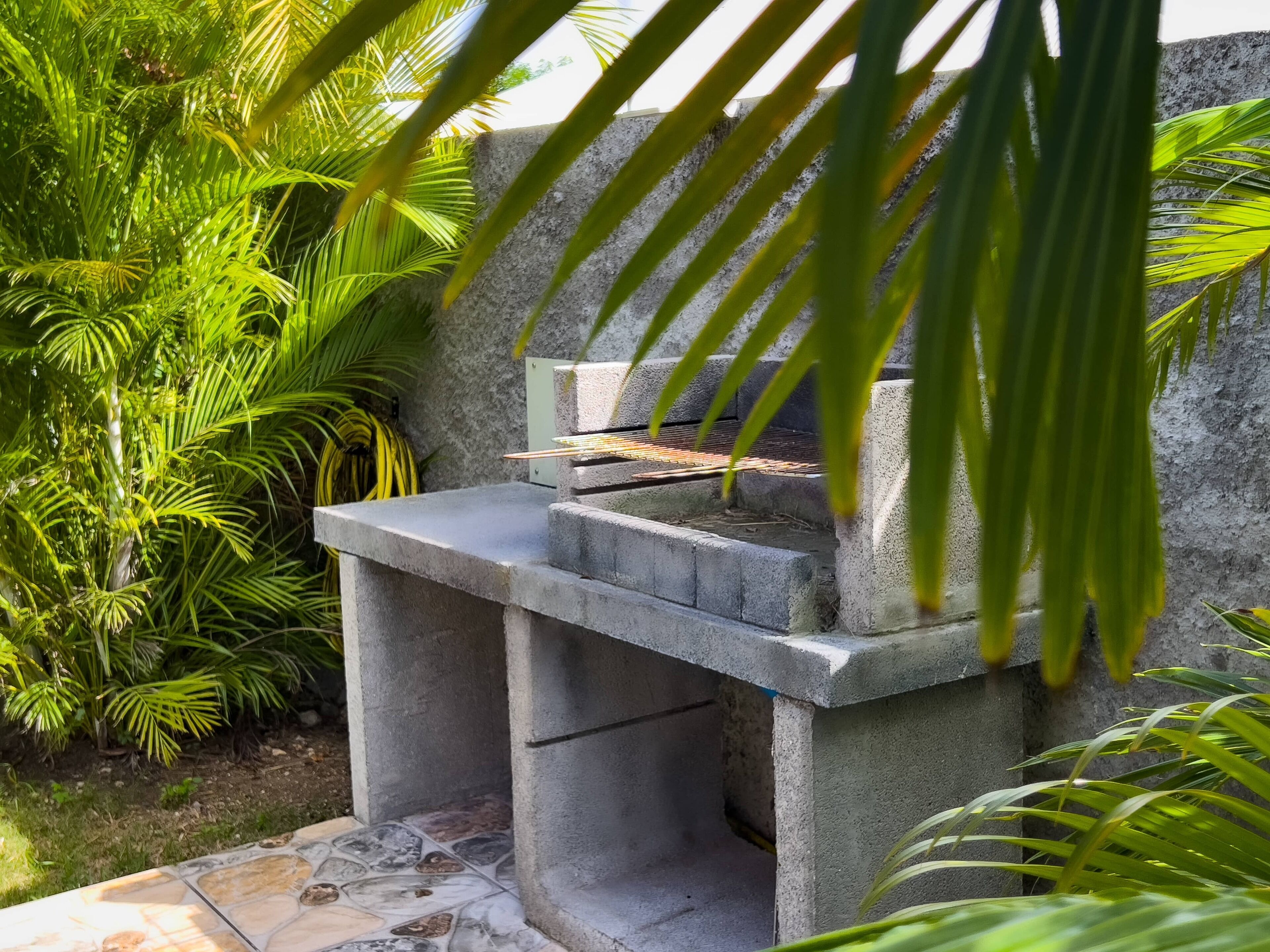 Una parrilla de concreto con base de piedra, rodeada de follaje verde exuberante.