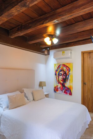 A bedroom with a wooden ceiling, a bed with white bedding, a painting on the wall, and an air conditioning unit. - Espectacular La Casita Cartagena (Cartagena)