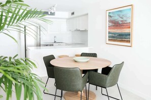 A modern kitchen with white cabinets, a central island, and a dining area with a round table and chairs.
