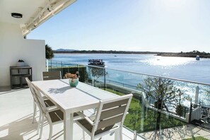 Varanda com mesa e cadeiras, vista para um rio com barcos.