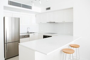 Una cocina moderna con armarios blancos, electrodomésticos de acero inoxidable y una isla central con taburetes.