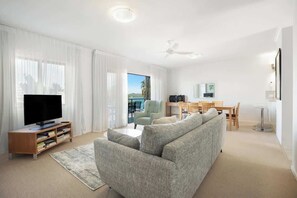 Ein modernes Wohnzimmer mit Flachbildfernseher, einem grauen Sofa und einem Essbereich mit Tisch und Stühlen.