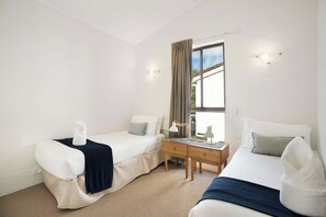 Quarto de hotel com duas camas, uma escrivaninha e uma janela com cortinas.