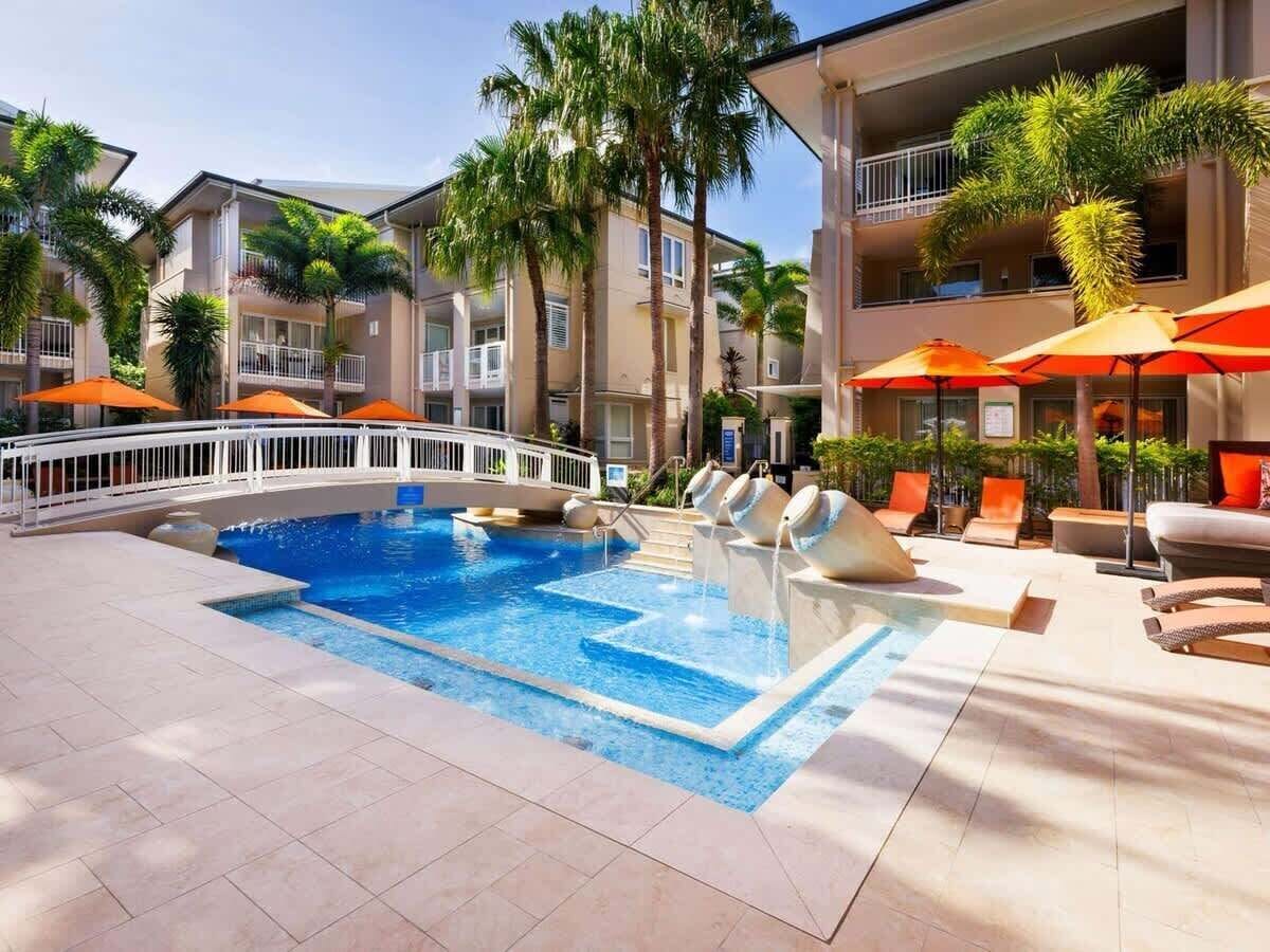 Área de piscina de hotel com piscina azul cristalina, espreguiçadeiras e guarda-sóis.