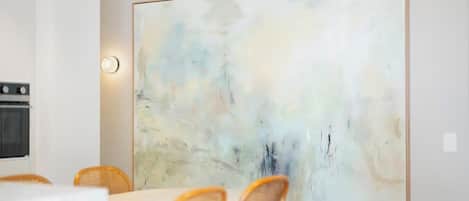 Un coin repas agrémenté d’un grand tableau abstrait au mur, d’une table ronde et de chaises en osier.