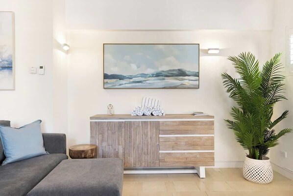 A modern living room with a grey sofa, a wooden console table, a large painting, and a potted plant.