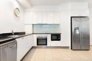 A modern kitchen with white cabinets, a stainless steel refrigerator, a built-in oven, and a microwave.