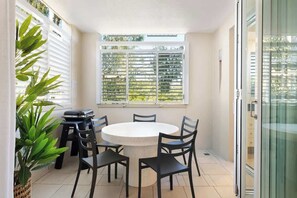 Um quarto com uma mesa redonda e cadeiras, um vaso de planta e uma janela com persianas.