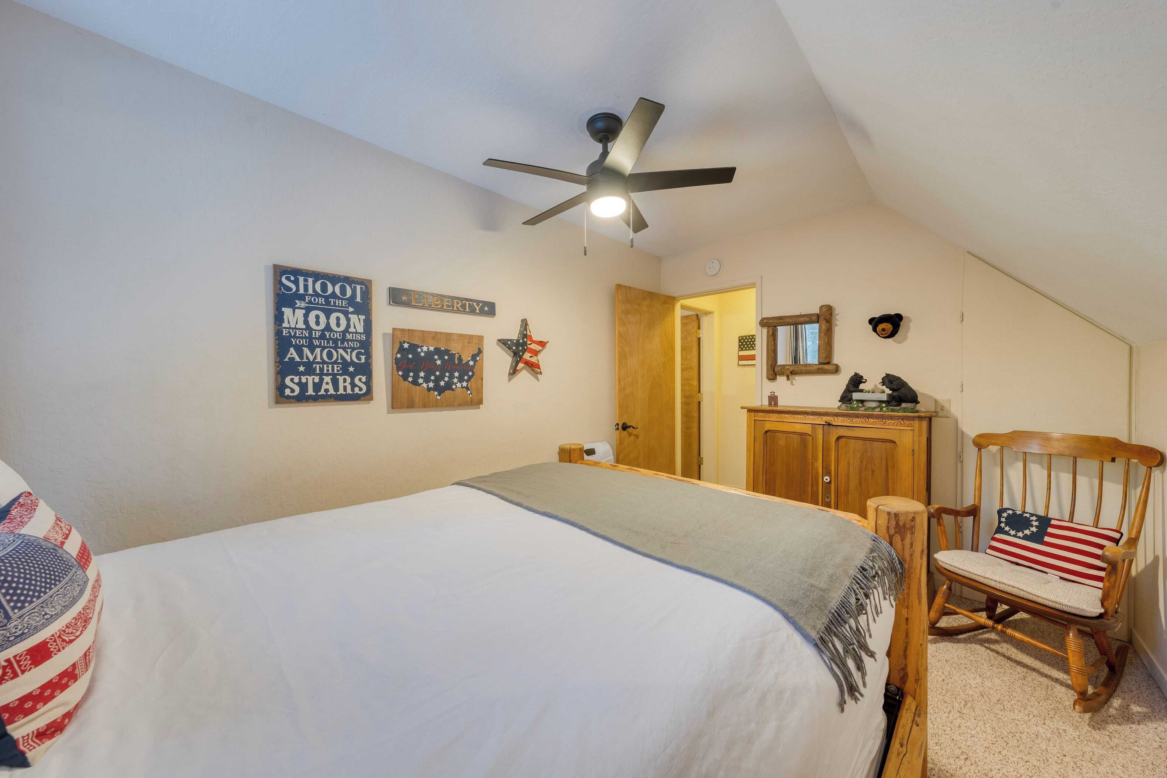 A bedroom with a bed, a wooden rocking chair, a ceiling fan, and wall decorations including a flag and a star.