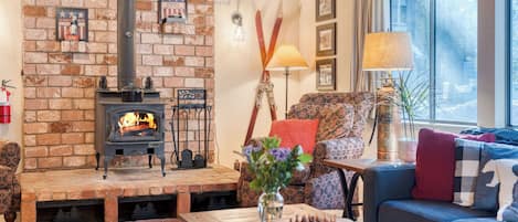 A cozy living room with a brick fireplace, a sofa, a table with a vase, and a window with curtains.