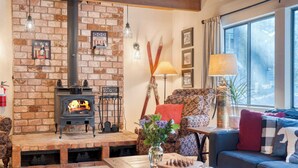 A cozy living room with a brick fireplace, patterned sofa, and a window with curtains. - Mountain Cabin w/ Fireplace, Balcony & Easy Ski Access Bear Americana (Truckee)