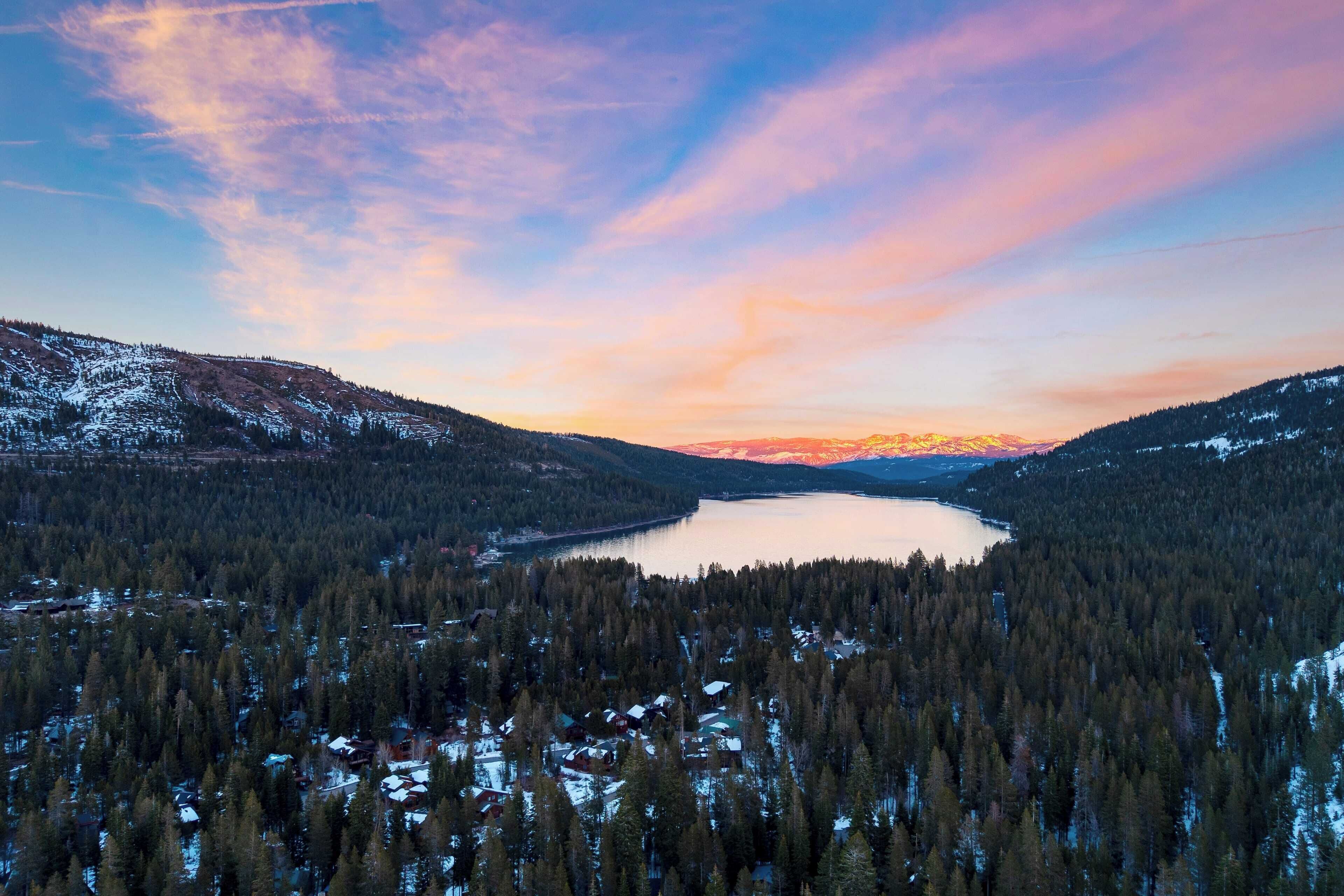 A mountainous landscape with a lake surrounded by dense forests and snow-covered peaks.