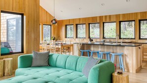 Une cuisine moderne avec un lambris en bois, un canapé vert et un coin bar avec des tabourets.