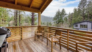 Une terrasse en bois avec un barbecue et des chaises, donnant sur une forêt et un chalet.
