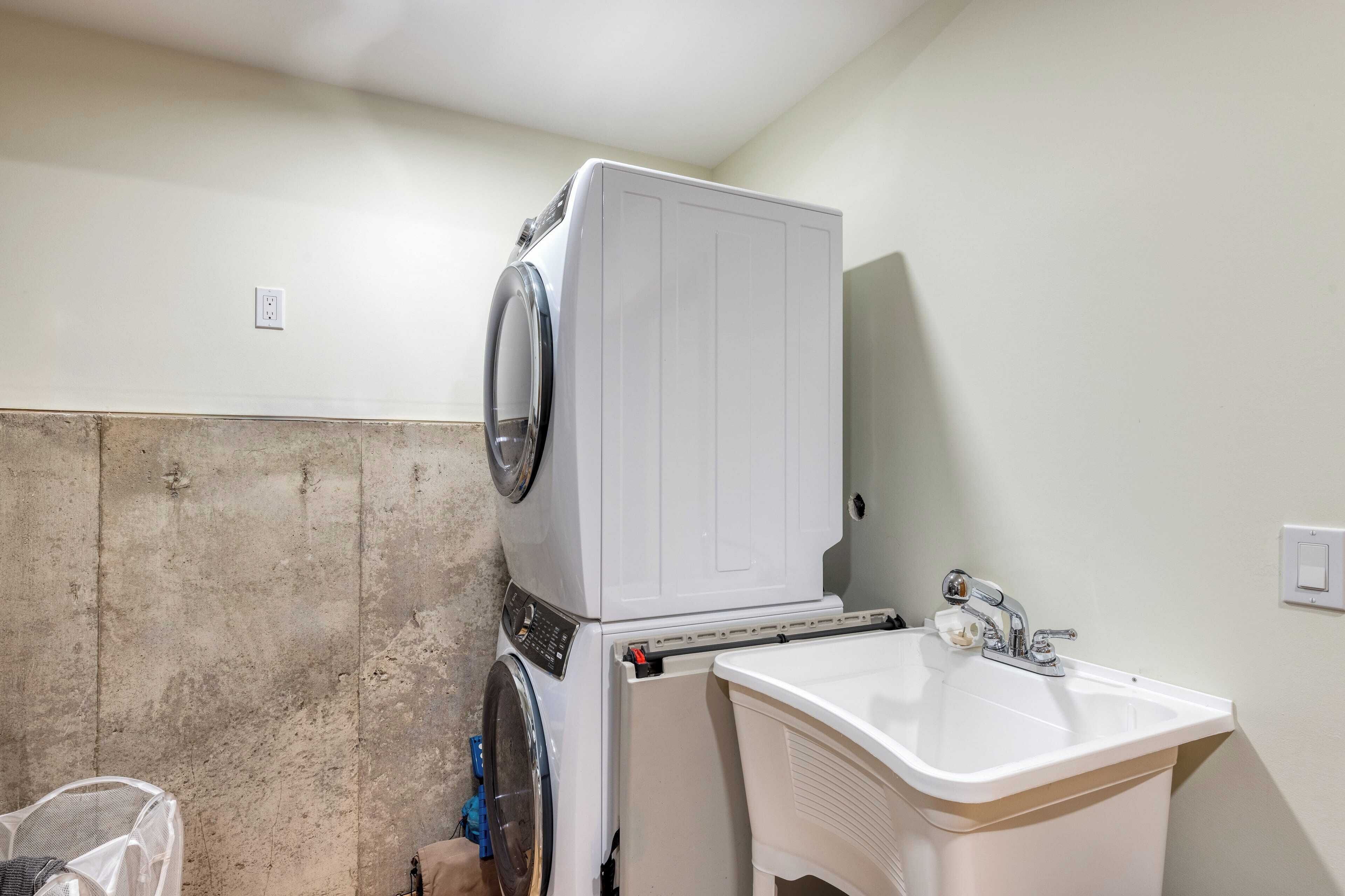 Une buanderie équipée d’un lave-linge et d’un sèche-linge superposés, d’un évier et d’une poubelle.