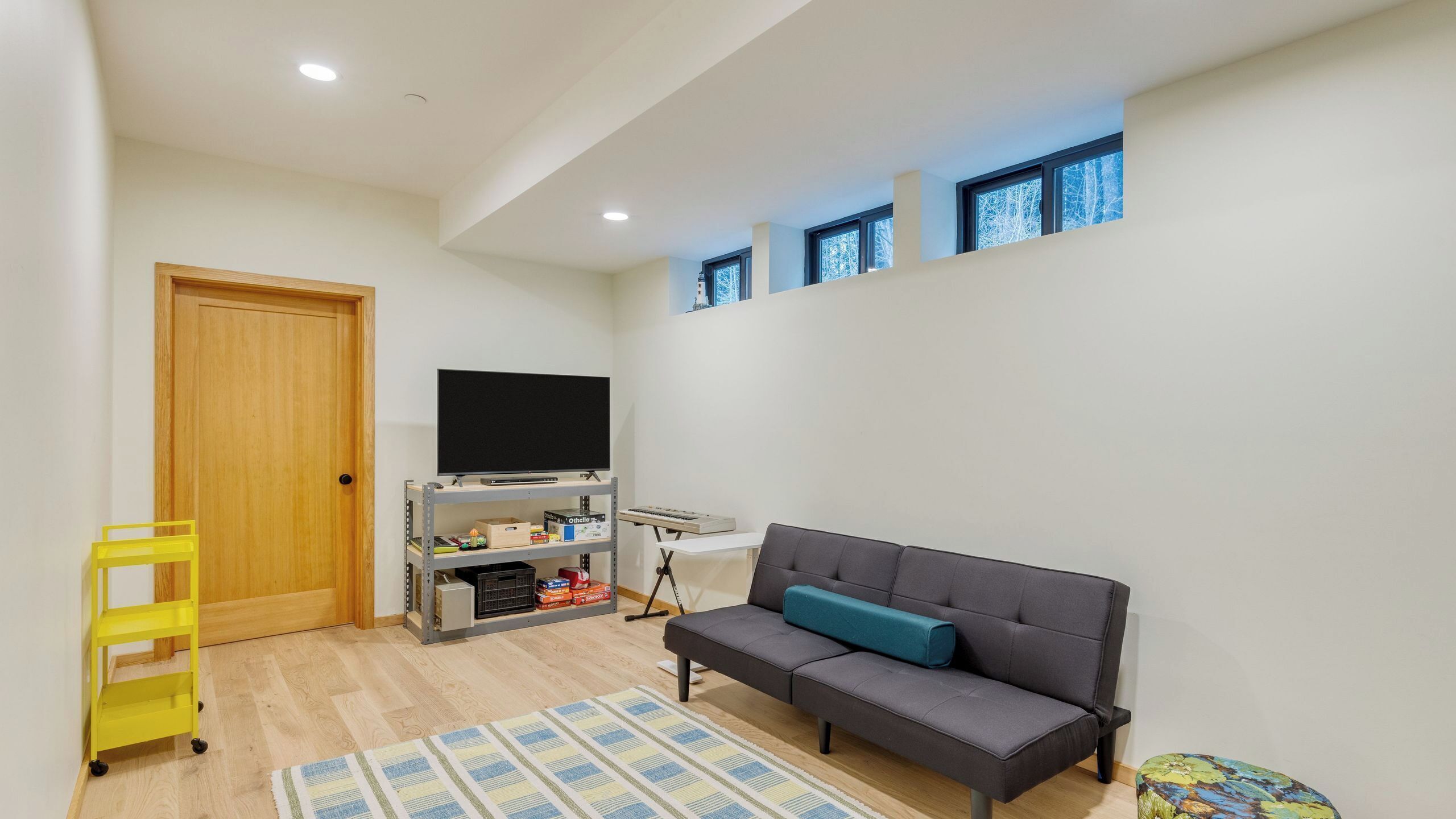 Una sala de estar con un sofá, un televisor, un estante con objetos, una puerta de madera y ventanas.