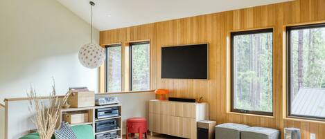 A modern living room with a green sofa, wooden walls, large windows, and a flat-screen TV mounted on the wall.