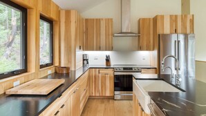 Une cuisine moderne dotée de meubles en bois, d’un réfrigérateur en acier inoxydable et d’une grande fenêtre offrant une vue sur l’extérieur.