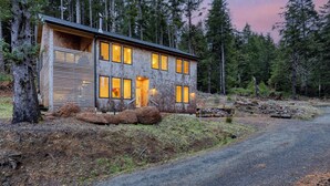 Une maison de style chalet moderne, avec un revêtement extérieur en bois, de nombreuses fenêtres et une allée gravillonnée.