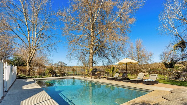 A rectangular swimming pool with a wooden deck, surrounded by lounge chairs and a covered umbrella. - Victorian Manor In Paso Robles Wine Country + Pool, Hot Tub, Firepit, Tennis Court Sleeps 28 (Paso Robles)