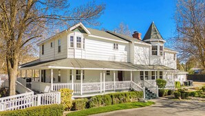 A two-story white house with a wrap-around porch, a turret, and a driveway. - Victorian Manor In Paso Robles Wine Country + Pool, Hot Tub, Firepit, Tennis Court Sleeps 28 (Paso Robles)